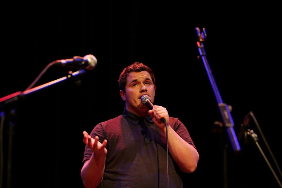 Forest Morgan, a young white man, performs Open Mic spoken word on stage.