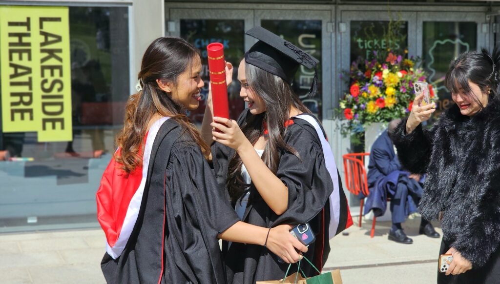 Essex graduation with two female graduands embracing outside the Lakeside Theatre